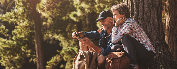 Hearing aid benefits - older man and woman outside by a try looking at a mobile phone