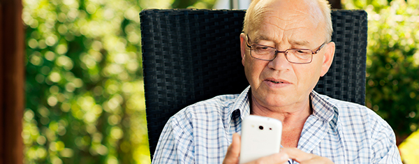 Hearing aid benefits - older man wearing glasses outside in chair on mobile phone