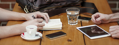 hearing loss - two people, man and woman, at a table across from one another with expresso, water, mobile phone and tablet